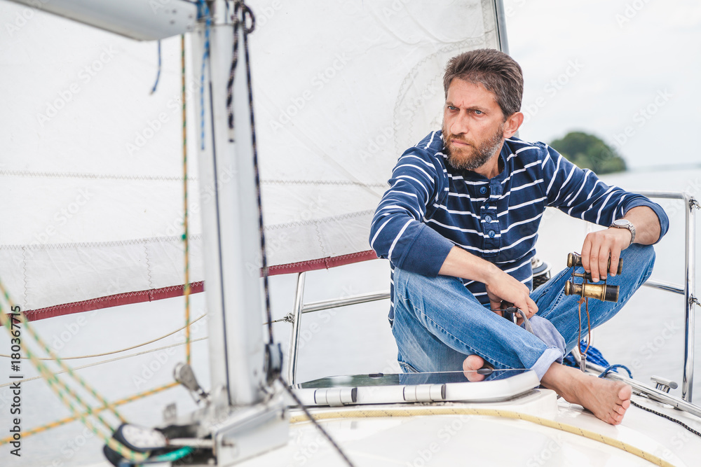 man sits on bow of sailing yacht and holds binoculars man sits on bow of sailing yacht and holds binoculars
