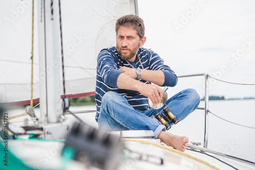 man sits on bow of sailing yacht and holds jar