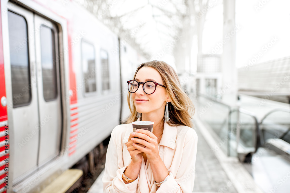 Portrait of a young elegant woman standing with coffee cup near the train at the railway station Portrait of a young elegant woman standing with coffee cup near the train at the railway station