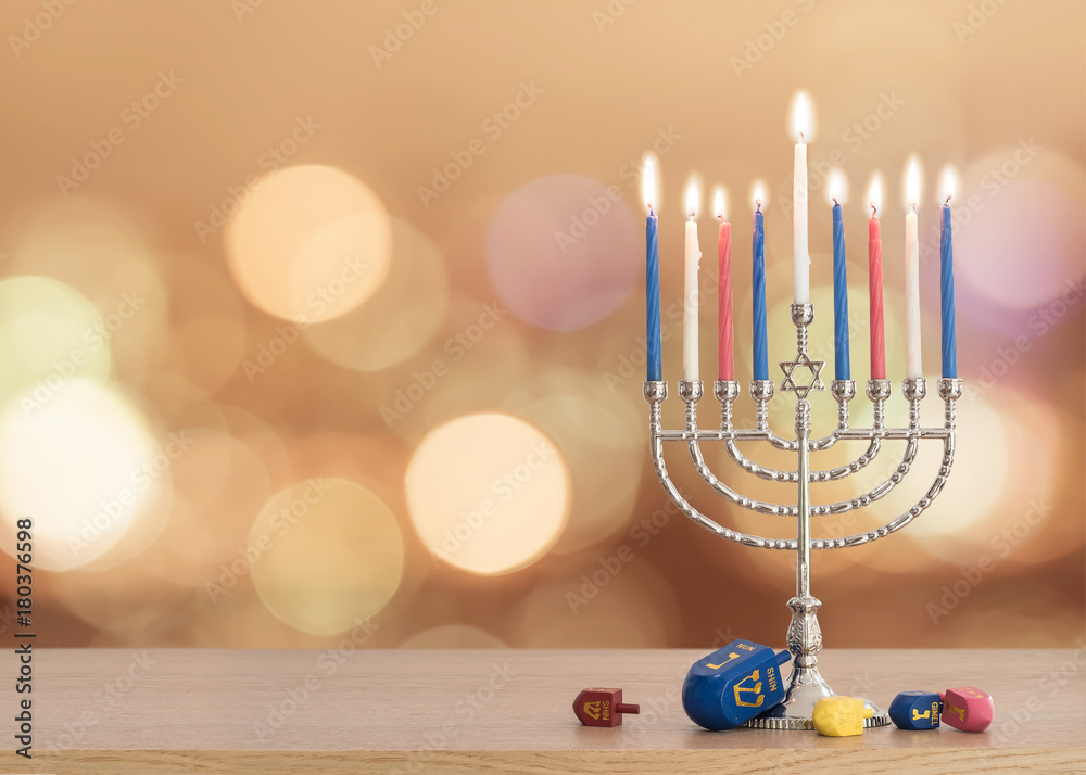 Fototapeta premium Hanukkah Jewish holiday background with menorah (Judaism candelabra) burning candles and traditional Dreidrel game toy on wood table and on autumn bokeh sun flare