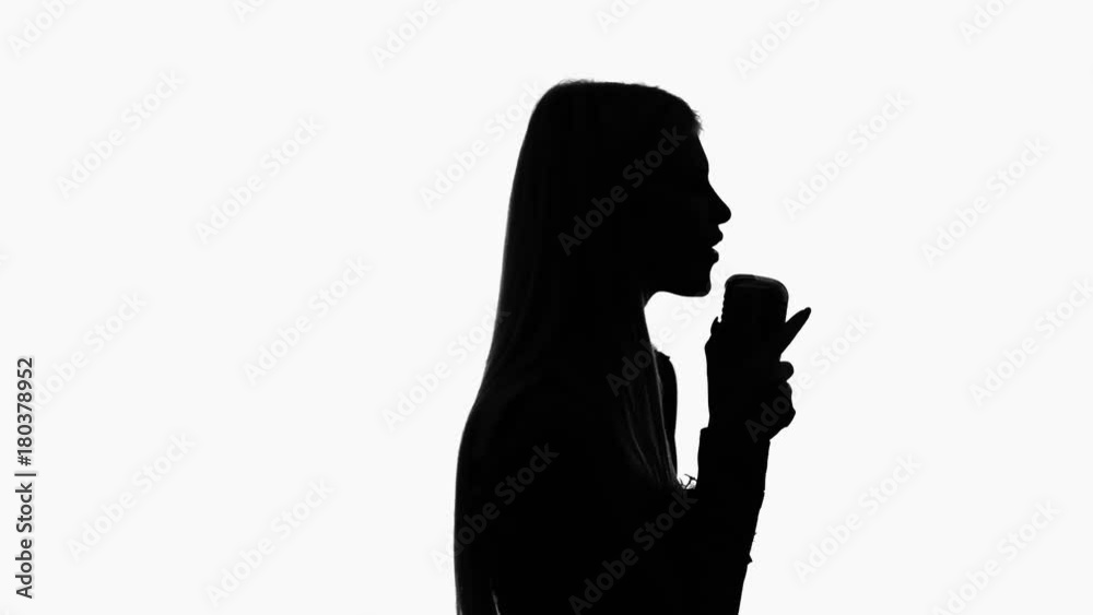 Vocalist in a dress is singing into a retro microphone. Silhouette. Side view. White background Vocalist in a dress is singing into a retro microphone. Silhouette. Side view. White background