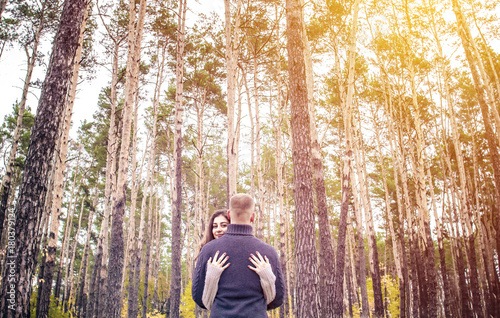 A beautiful girl stands embracing with a guy against the trees. Loving young couple. St. Valentine's Day.
