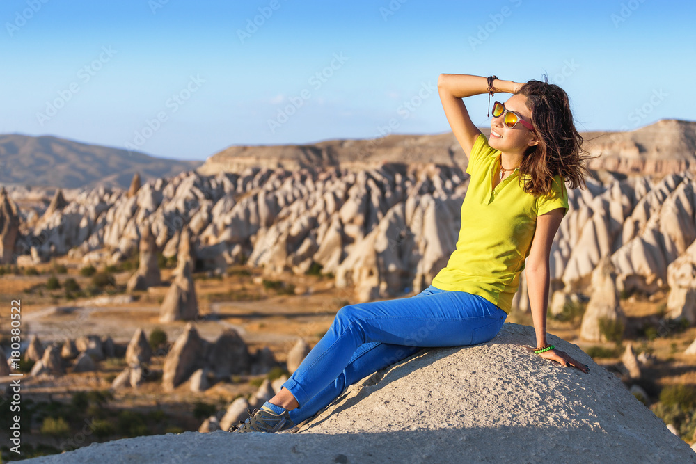 Naklejka premium A young tourist sitting on a mountain top and looking at the sunrise in Cappadocia at red valley. Tourism and travel in Turkey concept