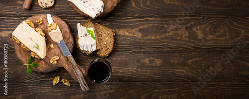 Assorted cheeses on wooden boards plate, bread and wine on dark wooden background, top view, flat lay, copy space, banner.