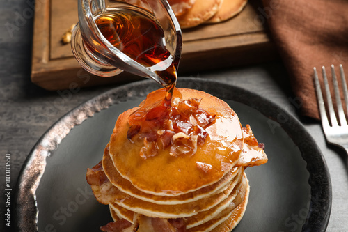 Pouring honey onto pancakes with bacon on plate
