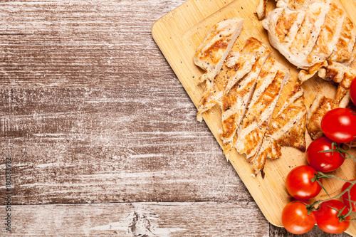 Delicious Fresh sliced grilled chicken breast on wooden board next to a bunch of tomatoes. Healthy dinner and lifestyle 