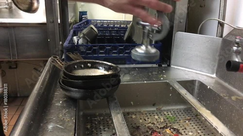 Restaurant worker sprays water onto pans and places them into washing area after a quick rinse. 