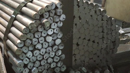 Industrial steel saw precisely cuts ends of stacked rods with tips falling as it moves.  