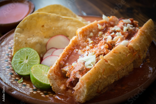 Authentic Mexican torta ahogada pork meat sandwich soaked in hot tomato sauce with lime and crispy tacos