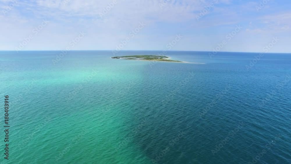 AERIAL: Small island in shallow waters of blue sea / Flying above shallow waters towards small island in blue sea, aerial view, drone point of view AERIAL: Small island in shallow waters of blue sea / Flying above shallow waters towards small island in blue sea, aerial view, drone point of view