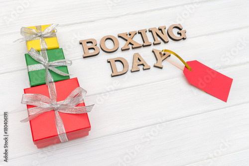 Above gift boxes is tied with a ribbon with words BOXING DAY and red tag on wood white background