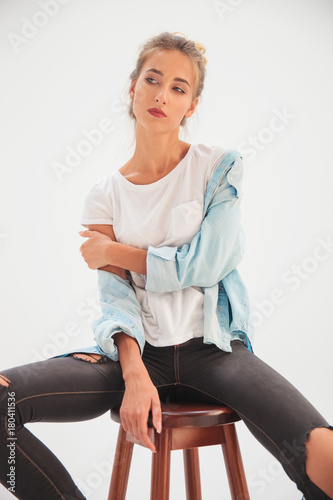 blonde casual woman sits on stool and looks to side