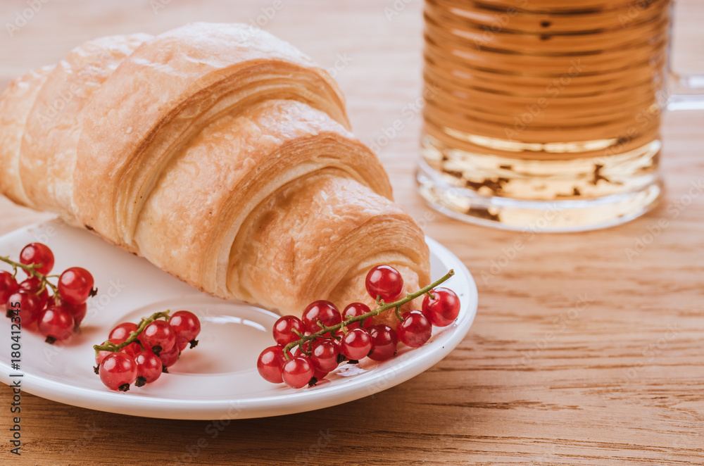 croissant with red berries and glass with tea/croissant with red berries in white bowl and glass with tea. Toned croissant with red berries and glass with tea/croissant with red berries in white bowl and glass with tea. Toned