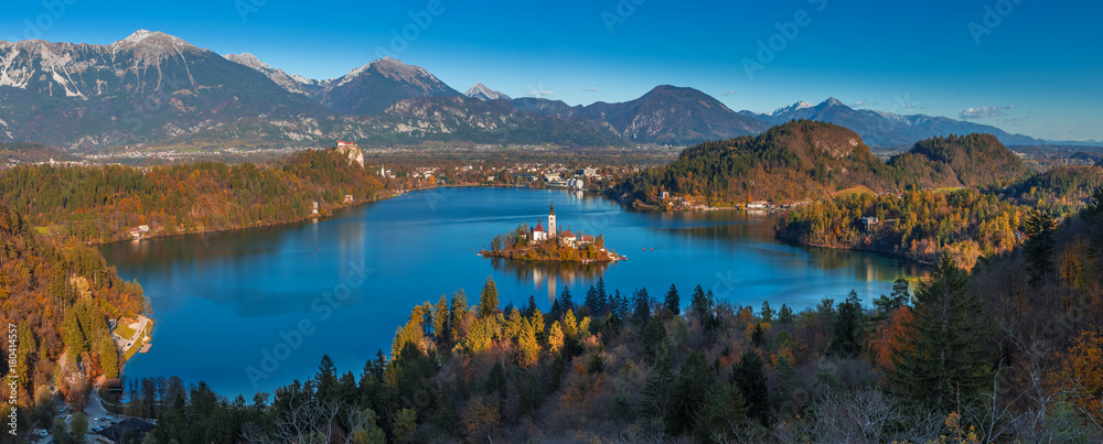 Obraz premium Bled, Słowenia - panoramiczny widok na jezioro Bled z punktu widokowego Ojstrica z kościołem pielgrzymkowym Wniebowzięcia Marii, tradycyjnymi łodziami Pletna i zamkiem Bled w tle jesienią