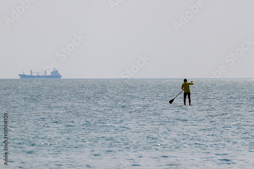 Silhouette of stand up paddle boarder paddling on a flat warm quiet sea © watcherfox