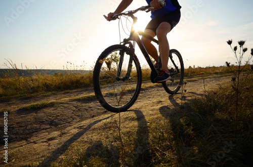 Fototapeta Naklejka Na Ścianę i Meble -  Male cyclist driving by rural dirt road outdoors. Low angle view