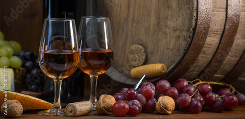 Glasses of rose wine cheeses grapesand barrel on brown wooden background