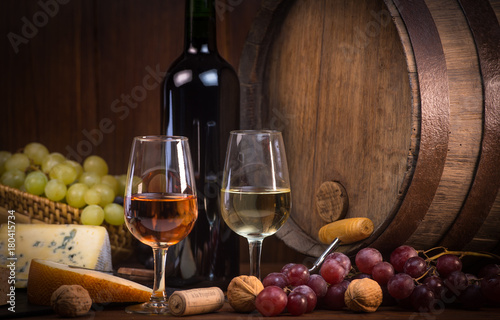 Glasses of rose and white wine cheeses grapesand barrel brown background