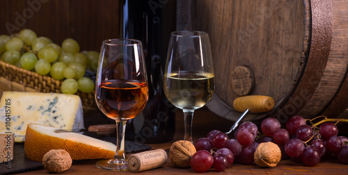 Glasses of rose and white wine cheeses grapesand barrel brown background