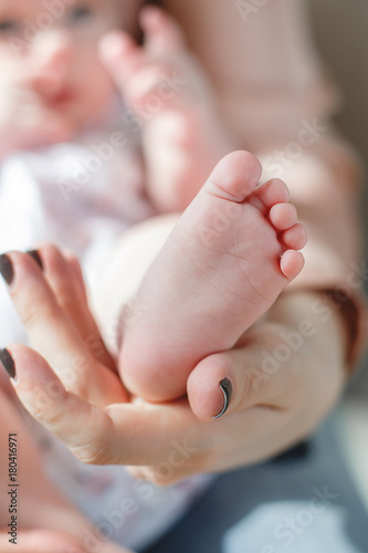 On the lap of a loving mother lies a newborn baby with fluffy little hair, mother gently supports the bare feet of the child with her hands,mother with a small son on the sofa concept of maternal love