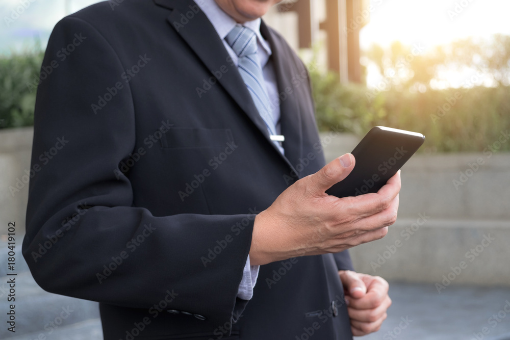 Attractive Confident businessman standing in a black suit and using smart phone to analyze investment Attractive Confident businessman standing in a black suit and using smart phone to analyze investment