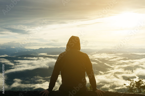 Traveller man sitting on the branch and viewing mist around the scenery with sun light in the morning.