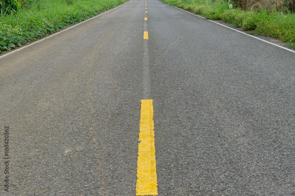 The yellow line on concrete road with green grass beside on this way The yellow line on concrete road with green grass beside on this way