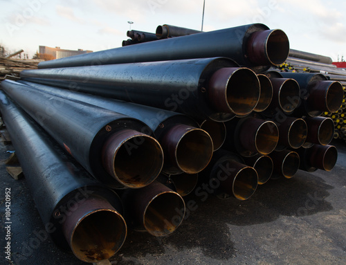 large black steel pipe with heat insulation on the construction site in a plastic tube wrapper lying on the pavement a bunch of horizontally. pipes for supplying gas or heat pressure medium