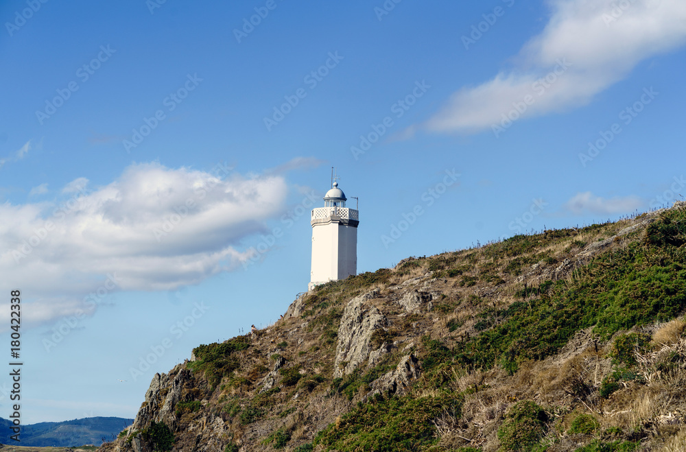 View of Mera lighthouse on a cliff on the atlantic coast of Spain in La Coruña. Sky with clouds and sun facing