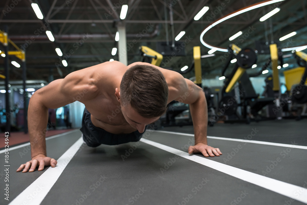 Fototapeta premium Portrait of young muscular man doing pushups on floor during workout in modern gym