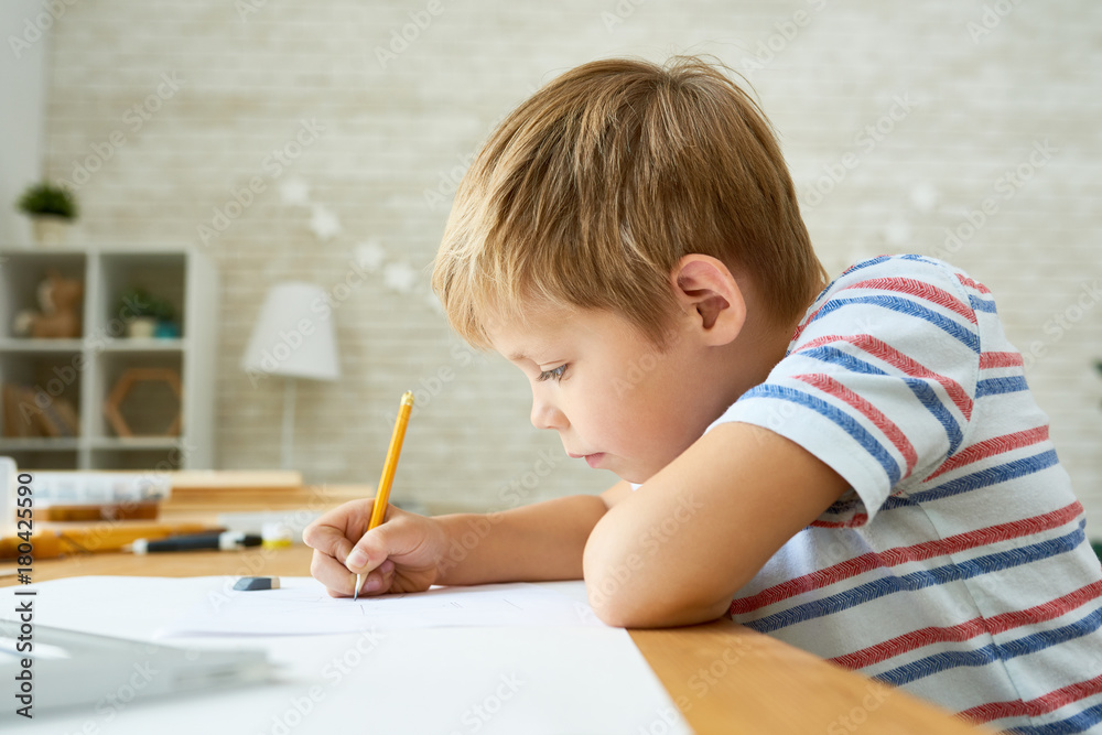 Side view portrait of diligent little boy writing or drawing carefully sitting at desk and doing homework, copy space Side view portrait of diligent little boy writing or drawing carefully sitting at desk and doing homework, copy space