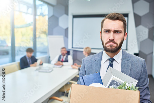 Portrait of sad bearded businessman holding box of personal belongings being fired from work in company, copy space