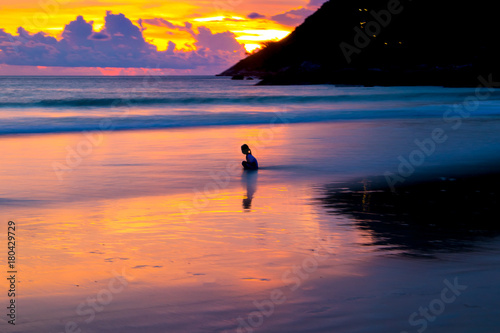 Silhouette little girl sitting alone lonely by the sea in the sunset time catch sea crabs.