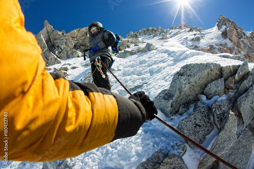 Tied climbers climbing mountain with snow field tied with a rope with ice axes and helmets first person