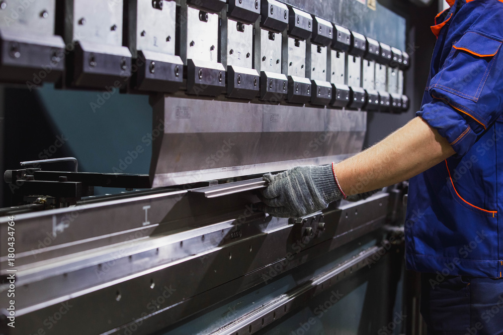 Man working with sheet metal on CNC hydraulic press brake. He puts the part and bends it into a large machine at an angle Man working with sheet metal on CNC hydraulic press brake. He puts the part and bends it into a large machine at an angle