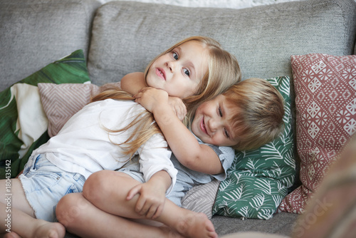 Foto Sweet shot of two adorable little sisters hugging on sofa in living room: baby g