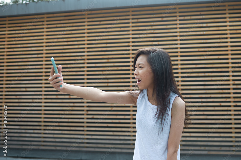 Picture of cheerful cute Vietnamese girl having video conference call with friend, using 3g or 4g internet connection on her mobile phone, opening mouth in excitement, extending arm with gadget in it Picture of cheerful cute Vietnamese girl having video conference call with friend, using 3g or 4g internet connection on her mobile phone, opening mouth in excitement, extending arm with gadget in it