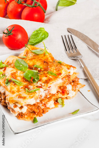 Italian food recipe. Dinner with classic lasagna bolognese with bechamel sauce, parmesan cheese, basil and tomatoes, on white marble table, coopy space