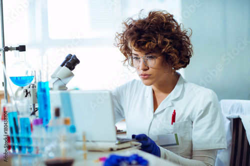 Portrait of confident female scientist working on laptop in chemical laboratory