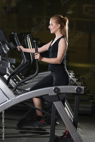Young woman at the gym exercising. Run on on a machine. Jogging workout in dark fitness club. Cardio.