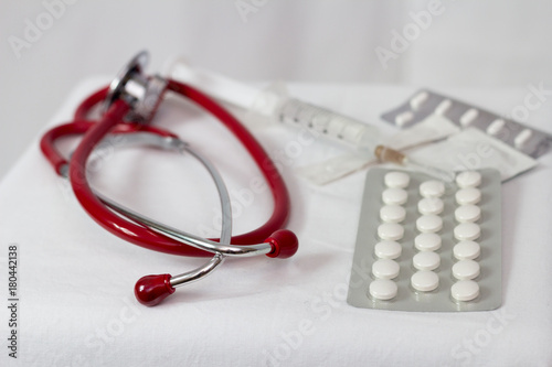 Czerwony stetoskop na białym tle pośród leków , strzykawek zbliżenie 