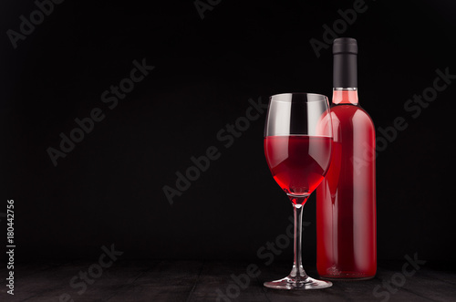Bottle of rose wine and wine glass mock up on elegant dark black wooden background, copy space.