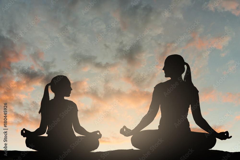 Silhouette of woman and her child doing yoga at sunset.