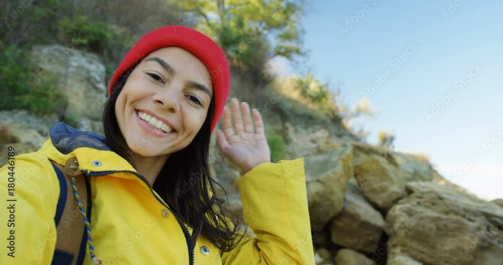 Close up of beautiful young woman in red hat having a video chatting on the rocky background. Cold but sunny day. Portrait. Outside. POV Close up of beautiful young woman in red hat having a video chatting on the rocky background. Cold but sunny day. Portrait. Outside. POV