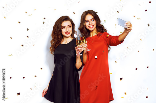 portrait of two happy young women who make selfie. in evening dresses on party over white background. firecrackers in the background.confetti.the concept party.funny faces
