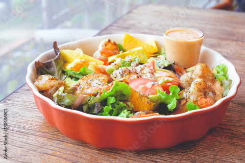 Fresh fruit salad with grilled shrimp and salad dressing served on red bowl.