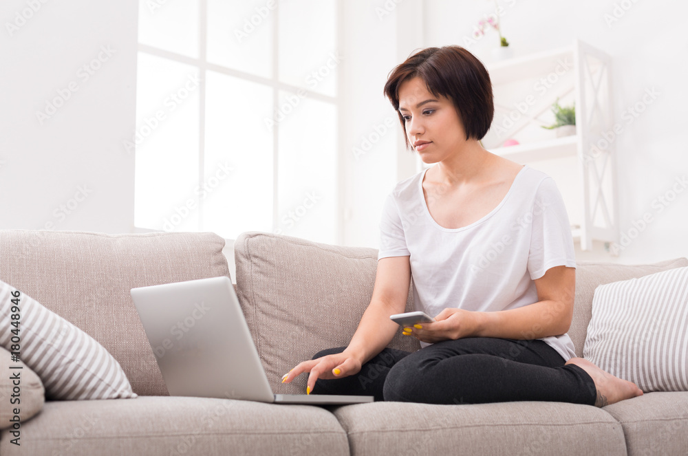 Pensive girl with laptop and mobile sitting on beige couch Pensive girl with laptop and mobile sitting on beige couch