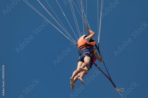 Two people on parachute flying over the beach, blue sky and sunny day