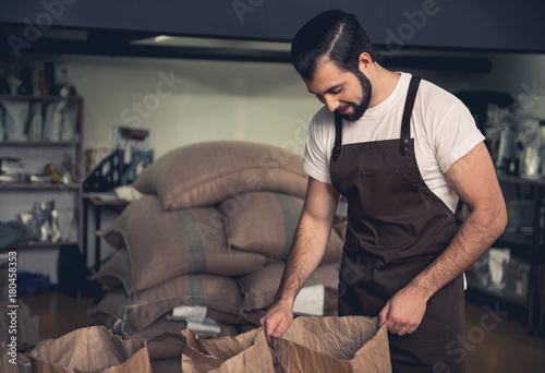 Side view happy unshaven young master keeping sack. He looking at coffee beans. Work concept