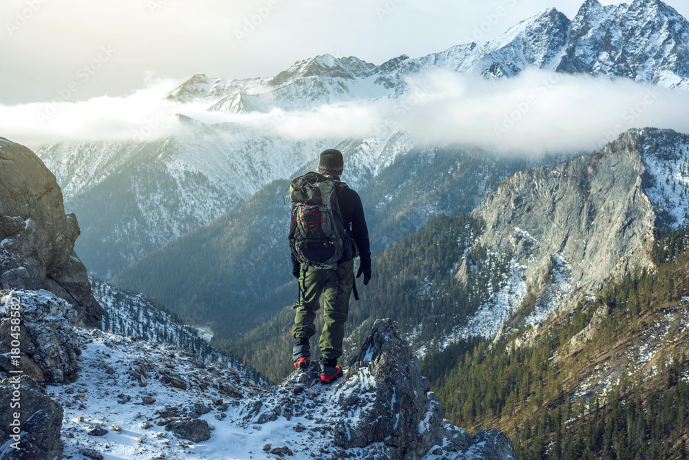 Naklejka premium Turysta mężczyzna z plecakiem na szczycie góry z tyłu, patrząc na stoku śniegu. Motywacja do koncepcji i osiąganie celów